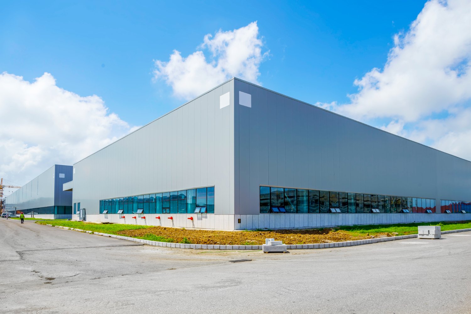 Modern industrial warehouse exterior with gray metal facade and blue glass windows under bright sky